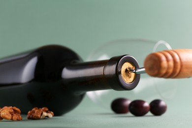 Wine bottle with corkscrew and walnuts on grey background, closeup