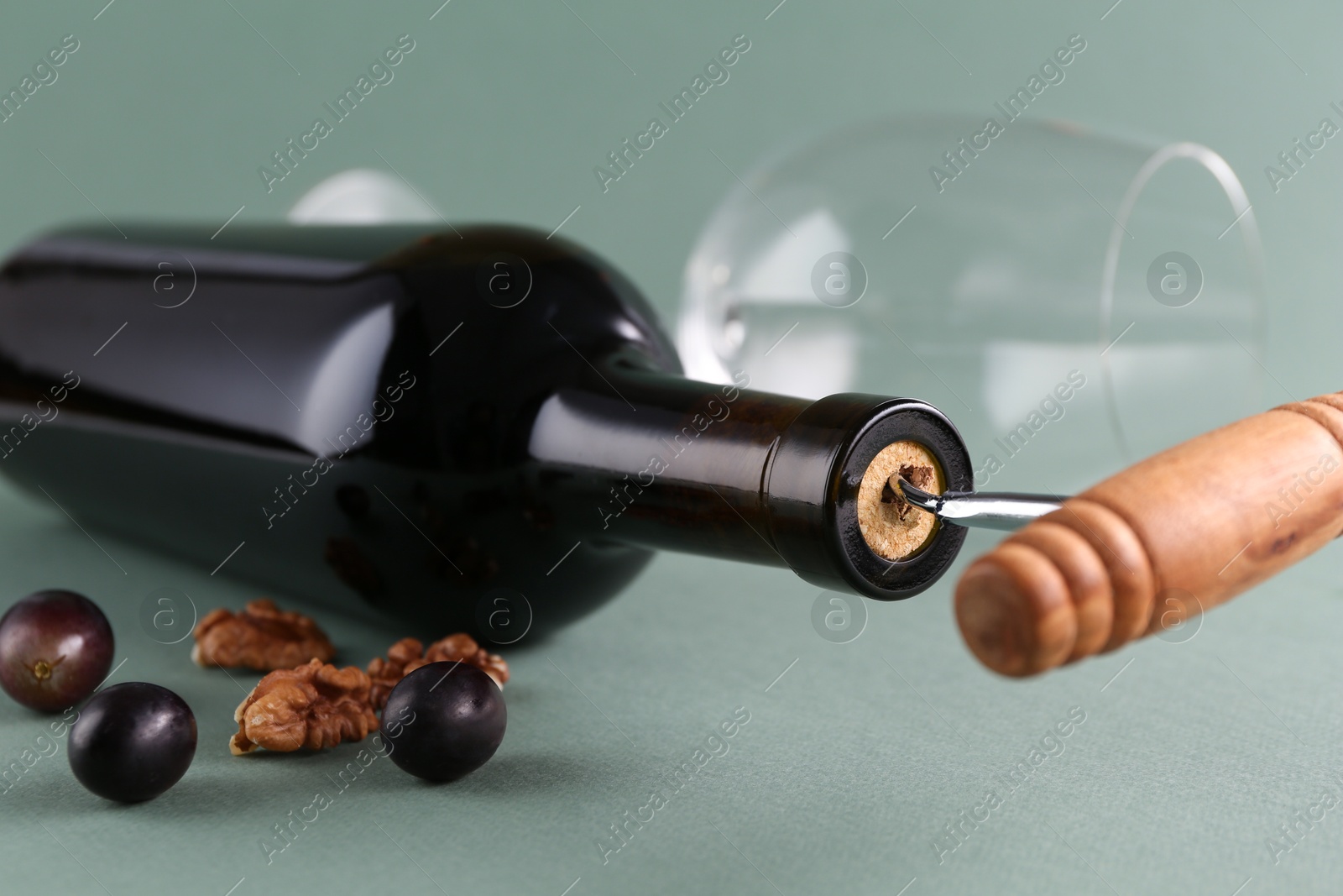 Photo of Wine bottle with corkscrew, grapes and walnuts on grey background, closeup