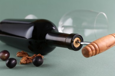 Wine bottle with corkscrew, grapes and walnuts on grey background, closeup