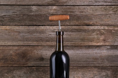 Wine bottle with corkscrew on wooden background