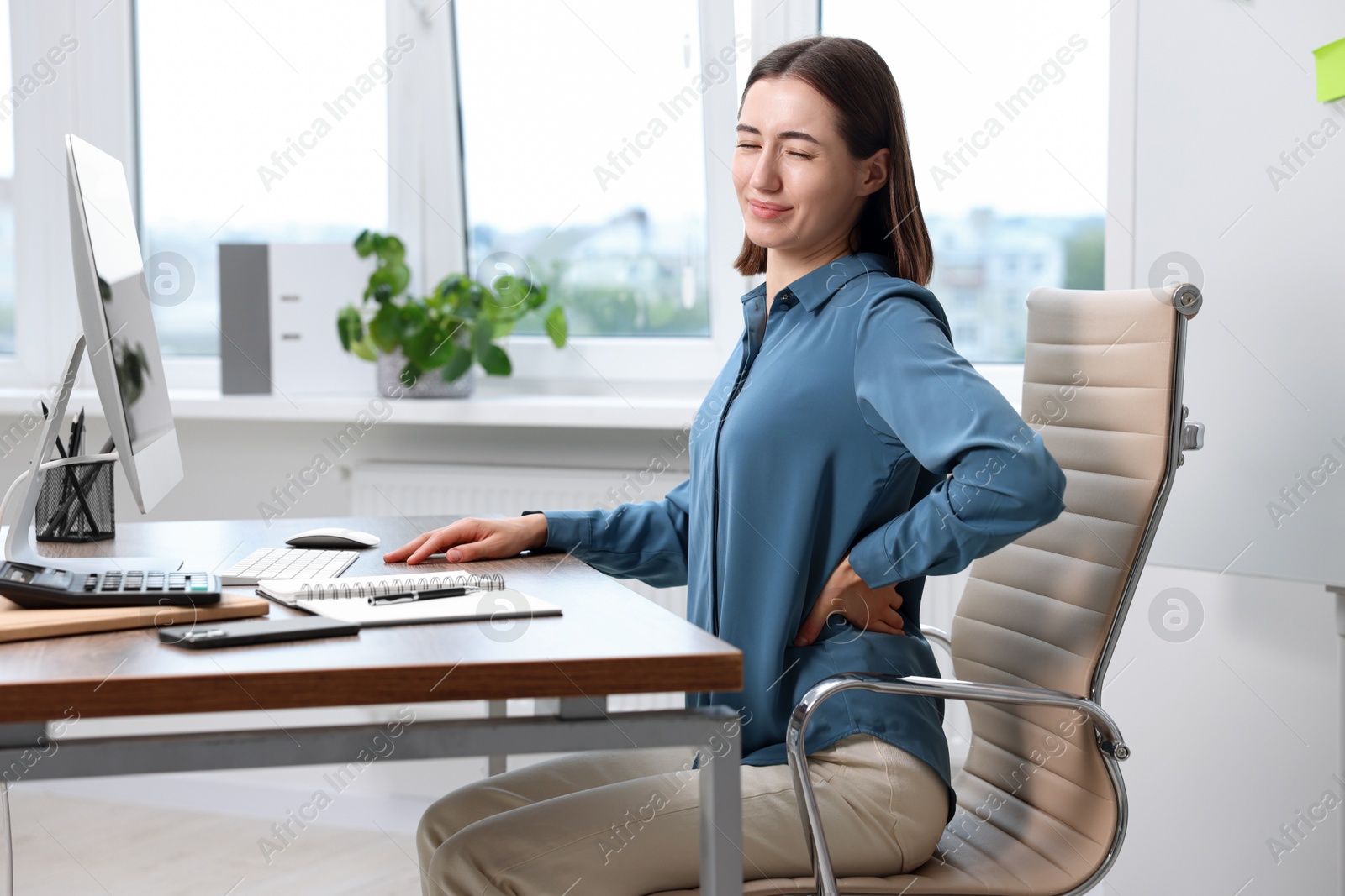 Photo of Woman suffering from back pain in office. Symptom of poor posture