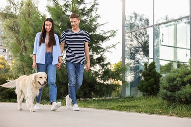 Photo of Happy couple walking with cute Golden Retriever dog outdoors, low angle view. Space for text