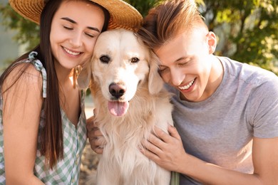 Happy couple with cute Golden Retriever dog outdoors on sunny day