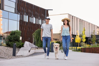 Happy couple walking with cute Golden Retriever dog outdoors