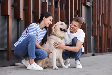 Photo of Happy couple stroking cute Golden Retriever dog outdoors