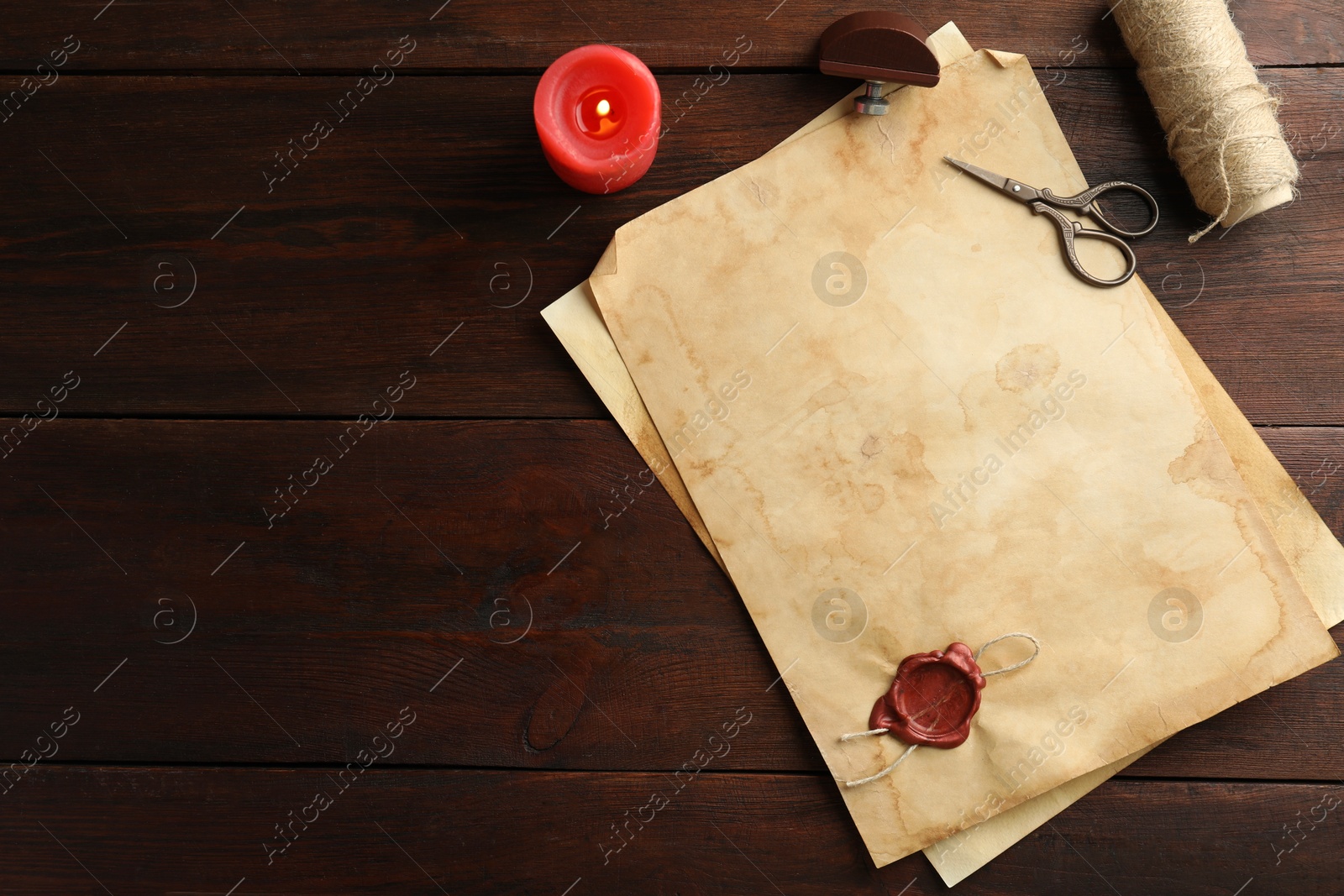 Photo of Sheet of old parchment paper with wax stamp, rope, scissors and candle on wooden table, flat lay