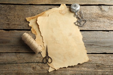 Sheet of old parchment paper, scissors, rope and pocket chain clock on wooden table, flat lay