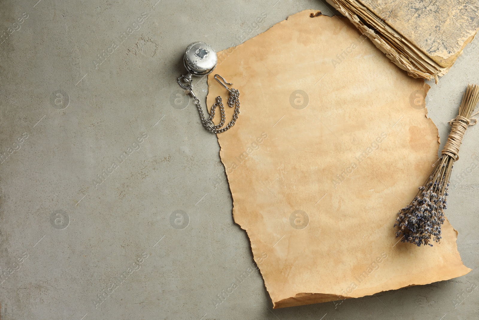 Photo of Sheet of old parchment paper, lavender flowers , vintage book and pocket chain clock on grey table, flat lay