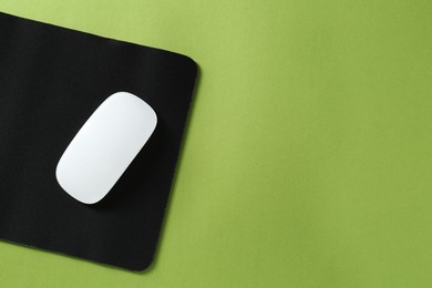 Wireless mouse and mousepad on green background, top view. Space for text