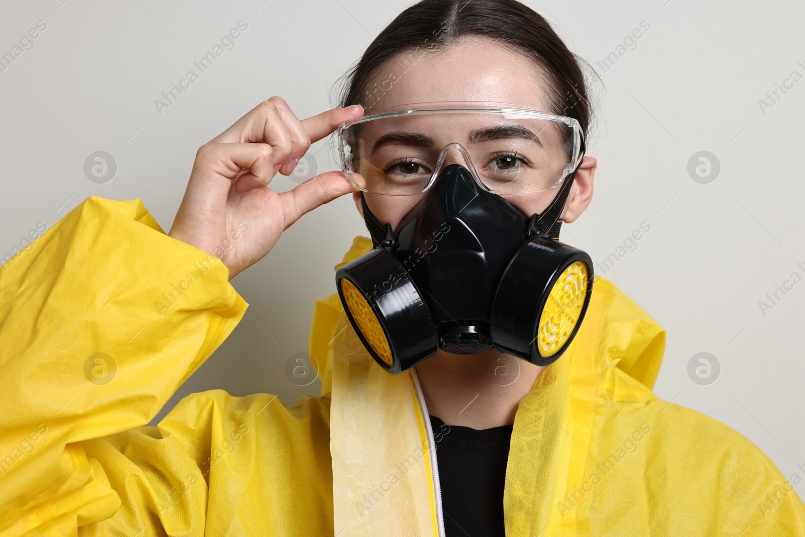 Photo of Worker in respirator, protective suit and glasses on grey background