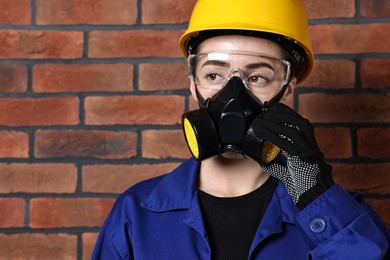 Photo of Worker in respirator, protective glasses and helmet near brick wall