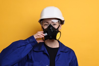 Photo of Worker in respirator, protective glasses and helmet on orange background