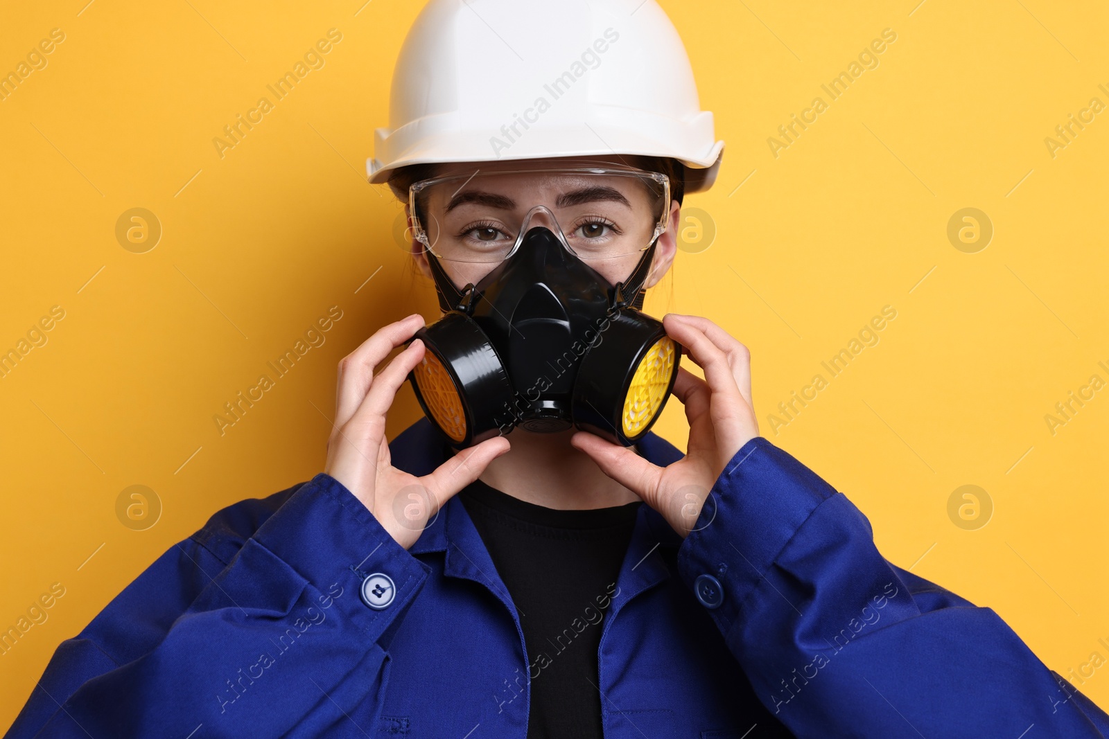 Photo of Worker in respirator, protective glasses and helmet on orange background