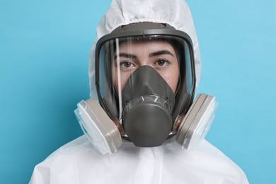 Photo of Worker in respirator and protective suit on light blue background