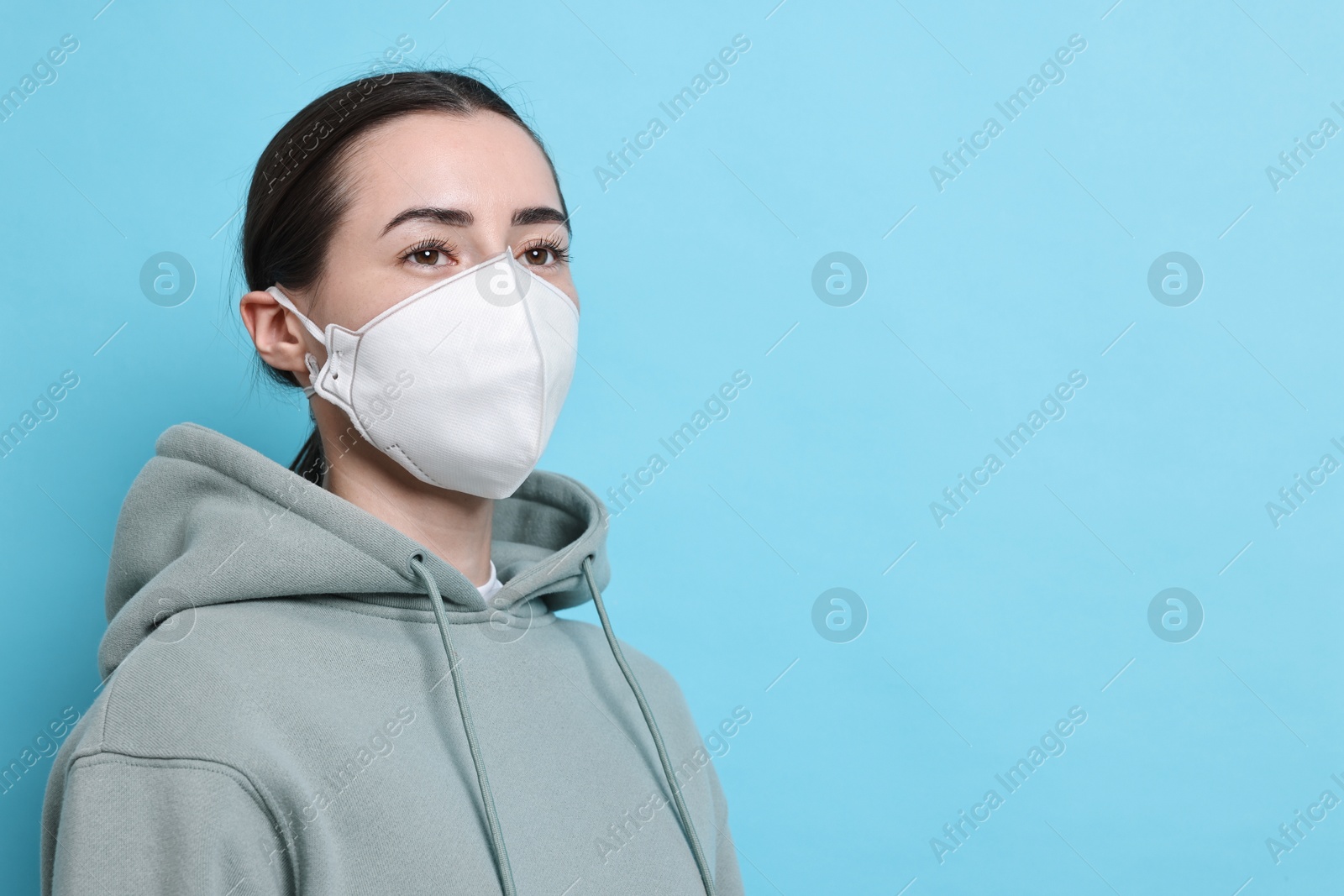 Photo of Woman in respirator mask on light blue background, space for text