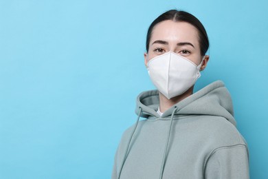 Photo of Woman in respirator mask on light blue background, space for text