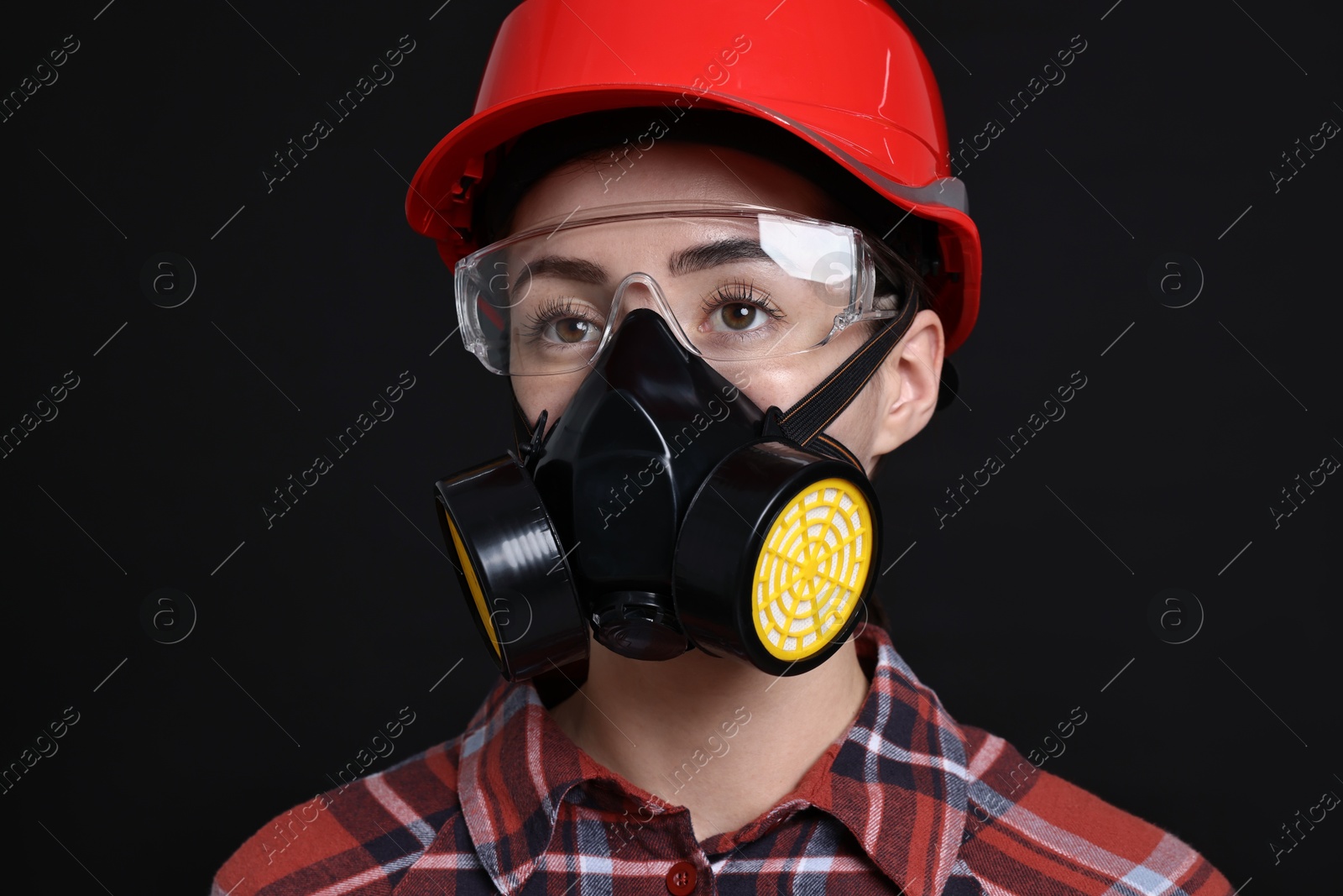 Photo of Woman in respirator, protective glasses and helmet on black background