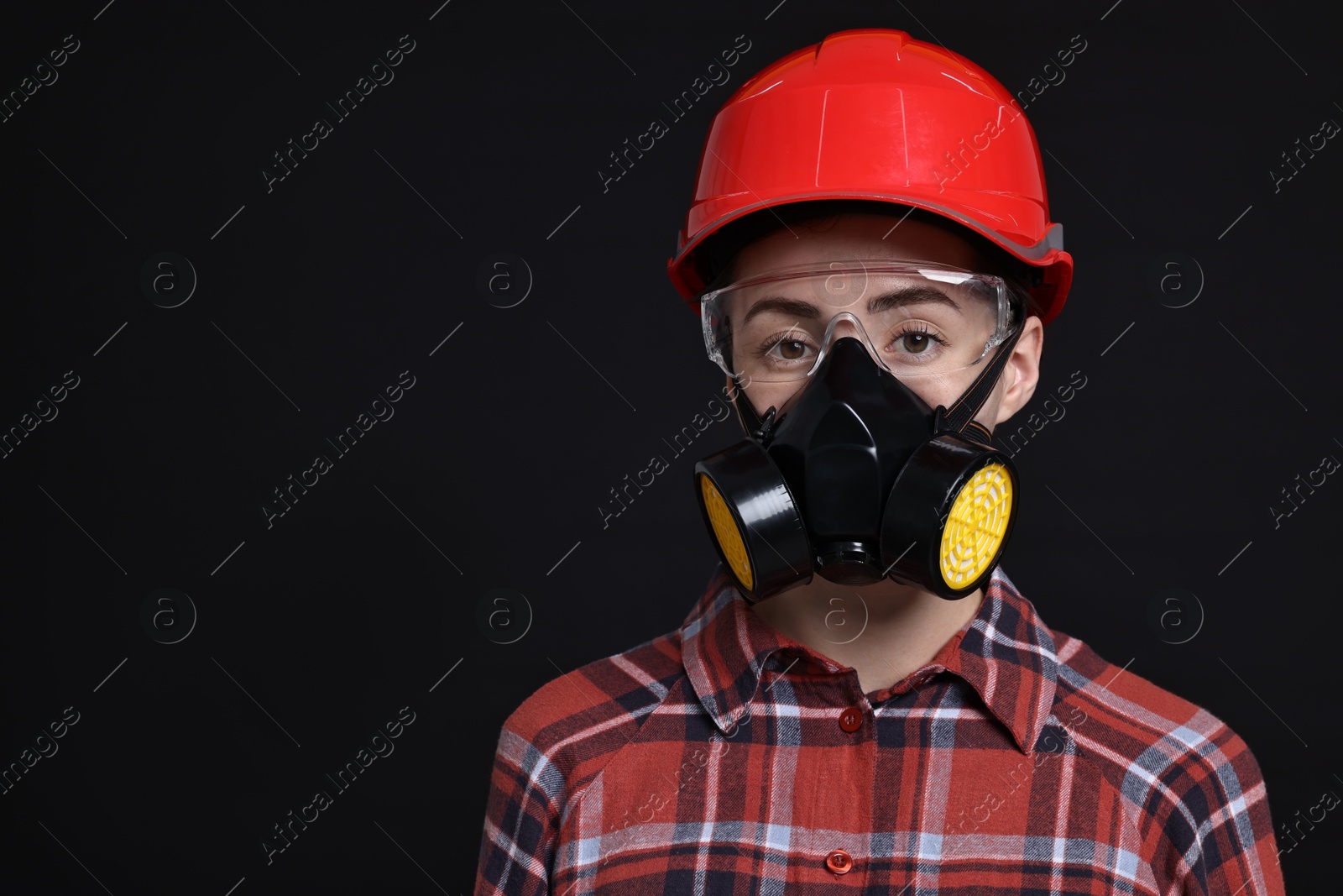 Photo of Woman in respirator, protective glasses and helmet on black background, space for text