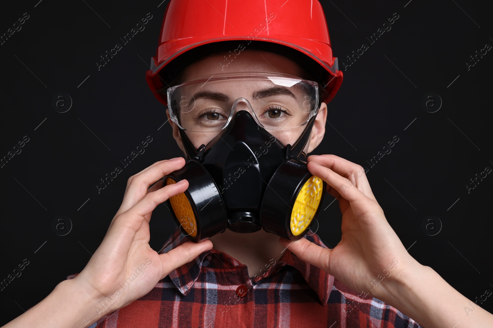 Photo of Woman in respirator, protective glasses and helmet on black background