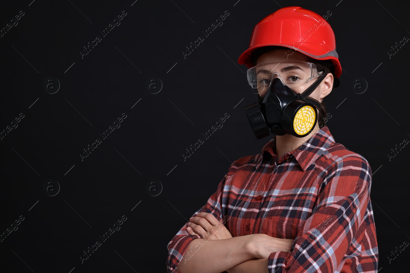 Photo of Woman in respirator, protective glasses and helmet on black background, space for text