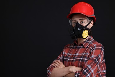 Photo of Woman in respirator, protective glasses and helmet on black background, space for text