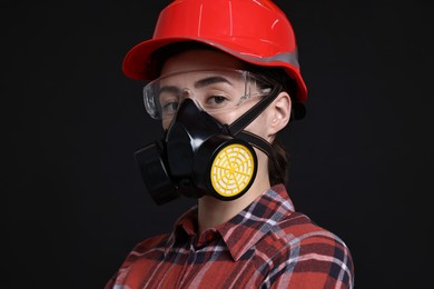 Photo of Woman in respirator, protective glasses and helmet on black background