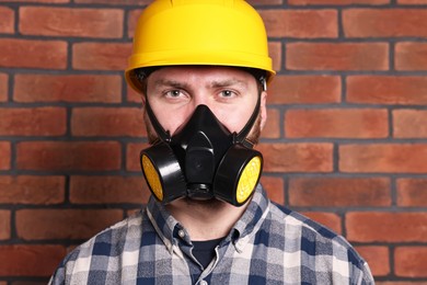 Photo of Man in respirator mask and hard hat near red brick wall