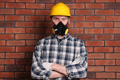 Man in respirator mask and hard hat near red brick wall