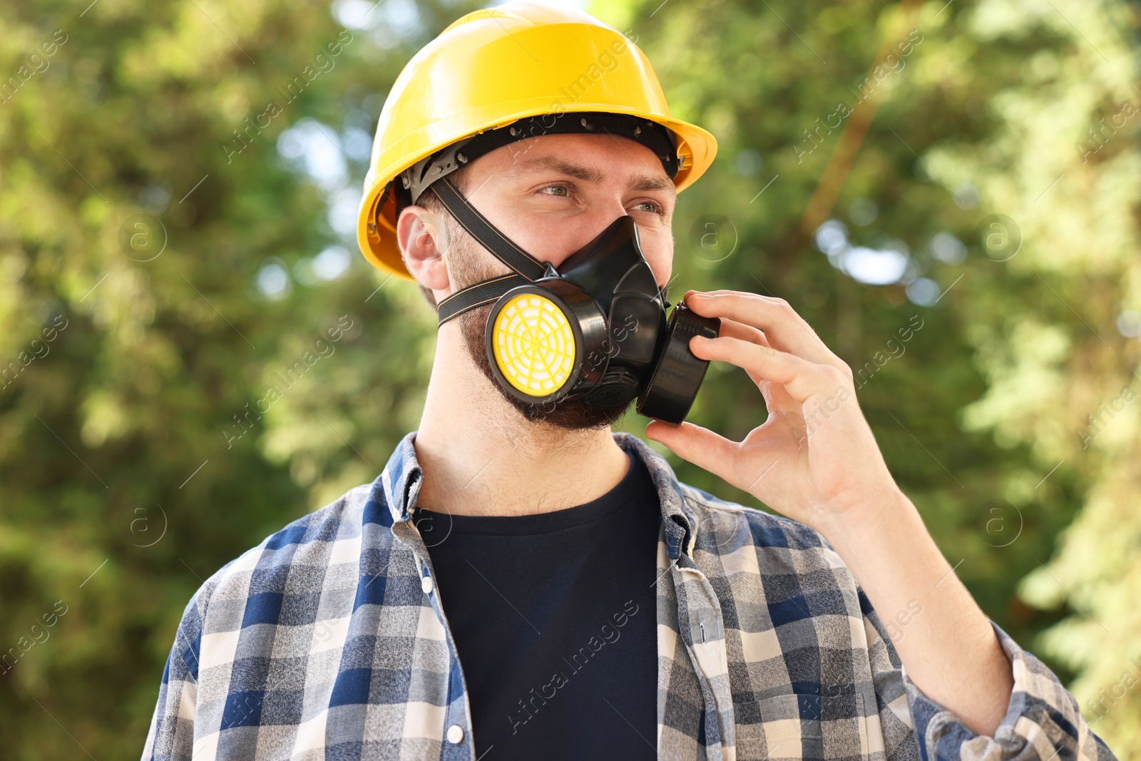 Photo of Man in respirator mask and hard hat outdoors. Safety equipment