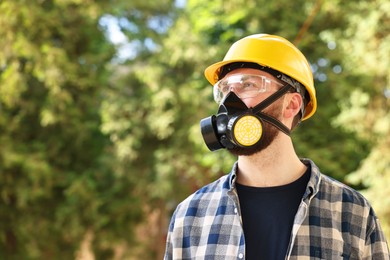 Man in respirator mask and hard hat outdoors, space for text. Safety equipment