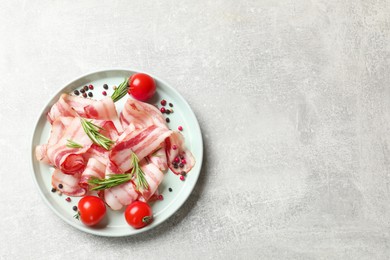 Photo of Slices of raw bacon, spices and tomatoes on light grey table, top view. Space for text