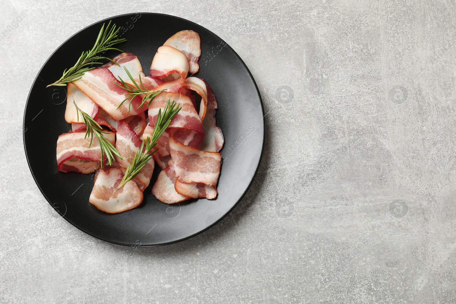 Photo of Slices of raw bacon and rosemary on light grey table, top view. Space for text