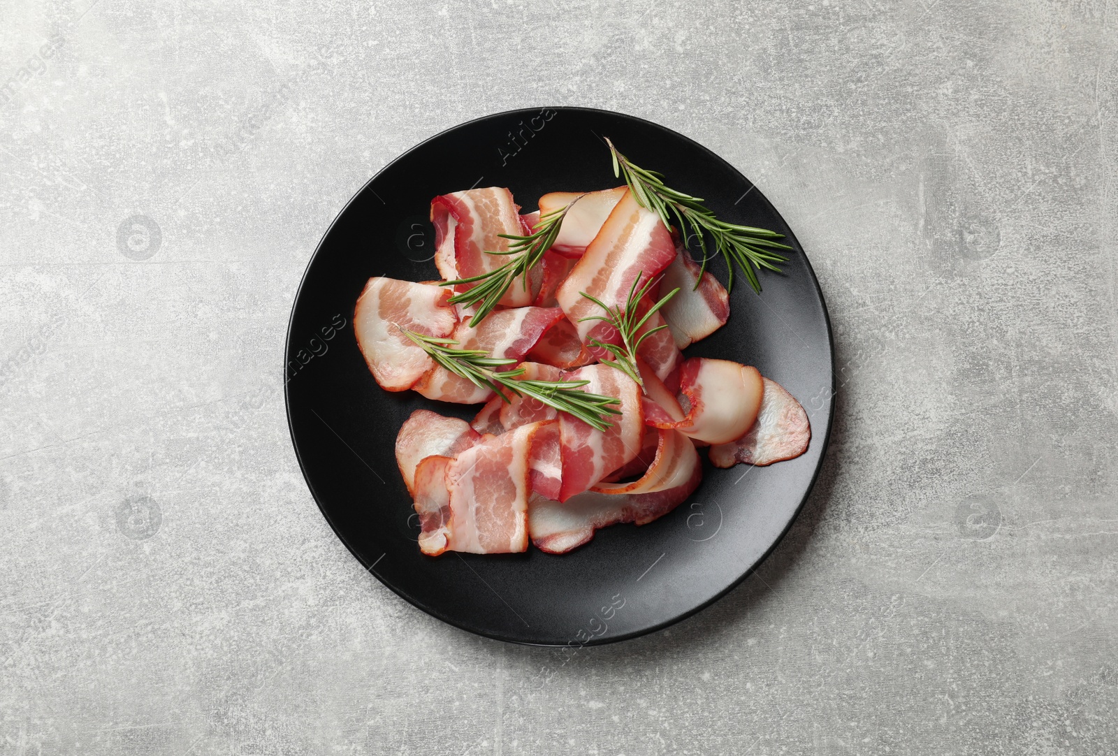 Photo of Slices of raw bacon and rosemary on light grey table, top view