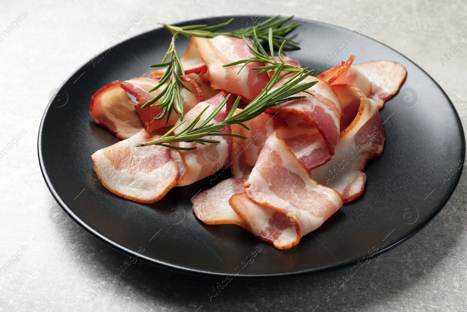 Photo of Slices of raw bacon and rosemary on light grey table, closeup