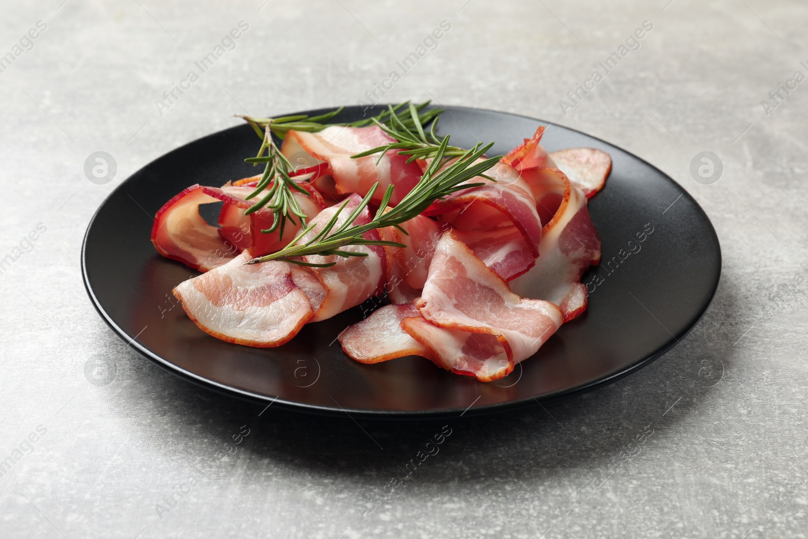 Photo of Slices of raw bacon and rosemary on light grey table