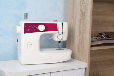 Photo of White sewing machine on nightstand near light blue wall indoors