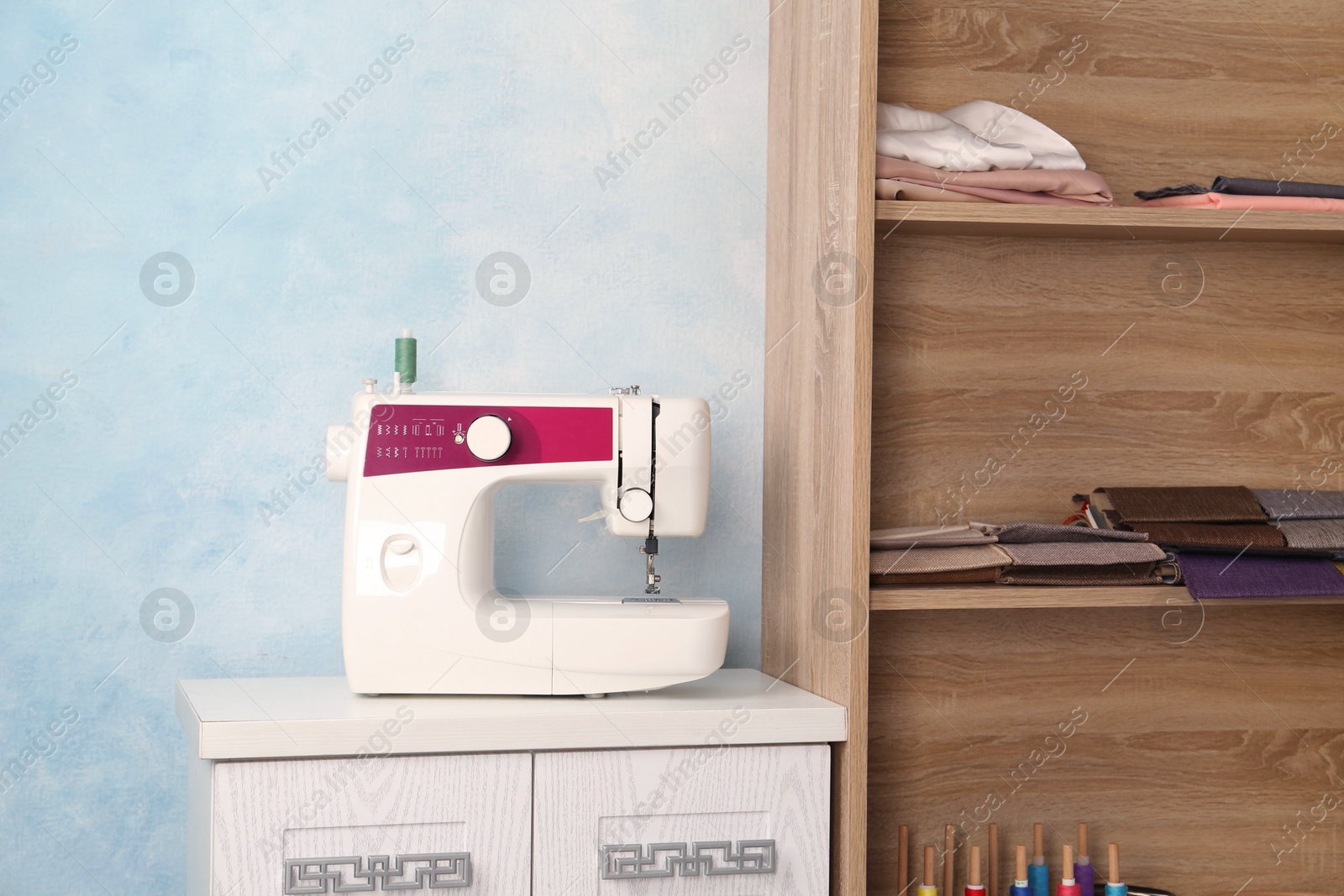 Photo of White sewing machine on wooden nightstand near light blue wall indoors