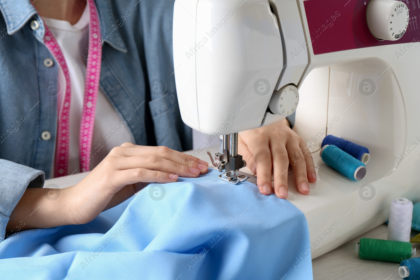 Photo of Seamstress working with sewing machine at table indoors, closeup