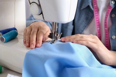 Photo of Seamstress working with sewing machine at table indoors, closeup