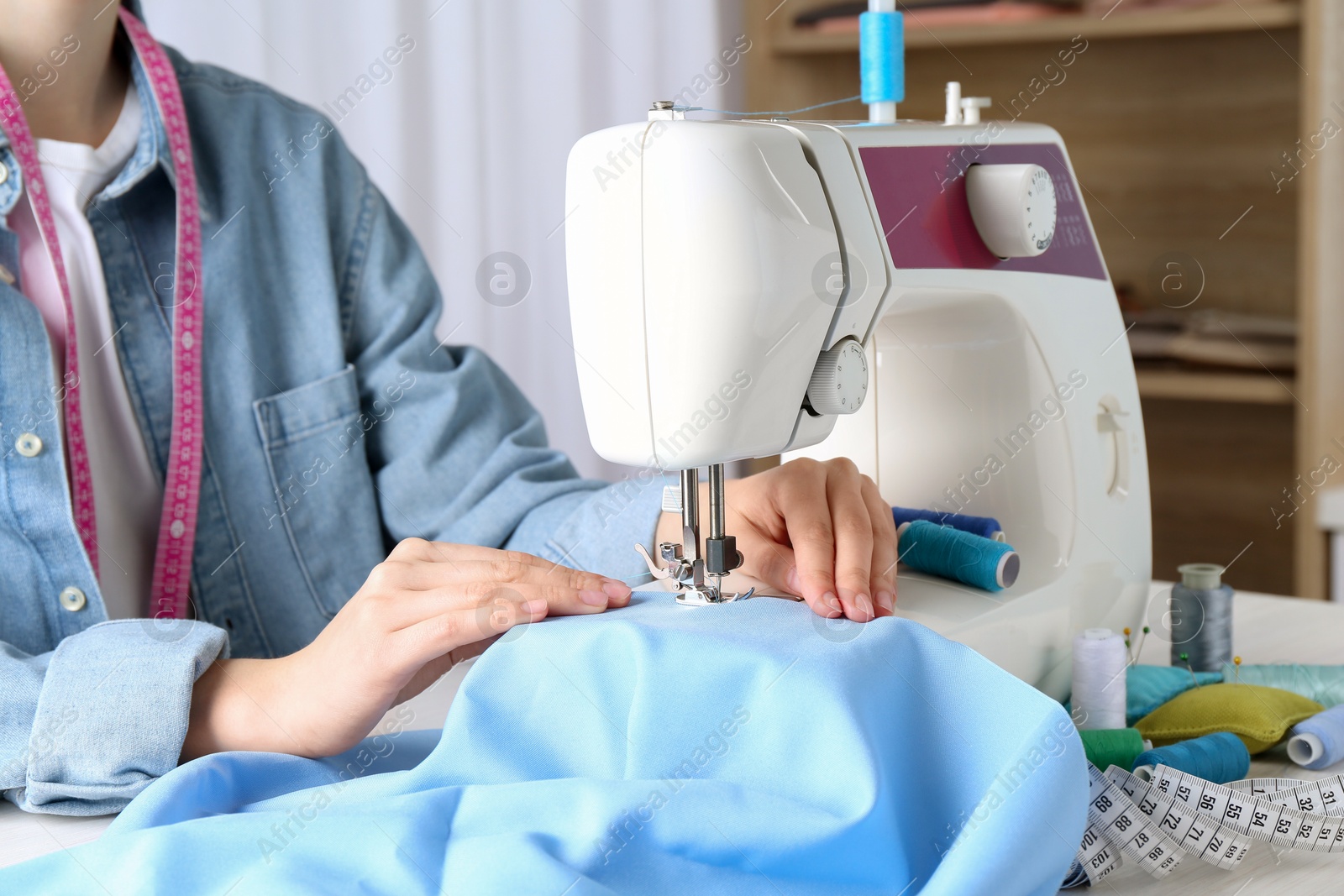 Photo of Seamstress working with sewing machine at table indoors, closeup