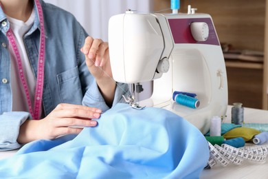 Photo of Seamstress working with sewing machine at table indoors, closeup