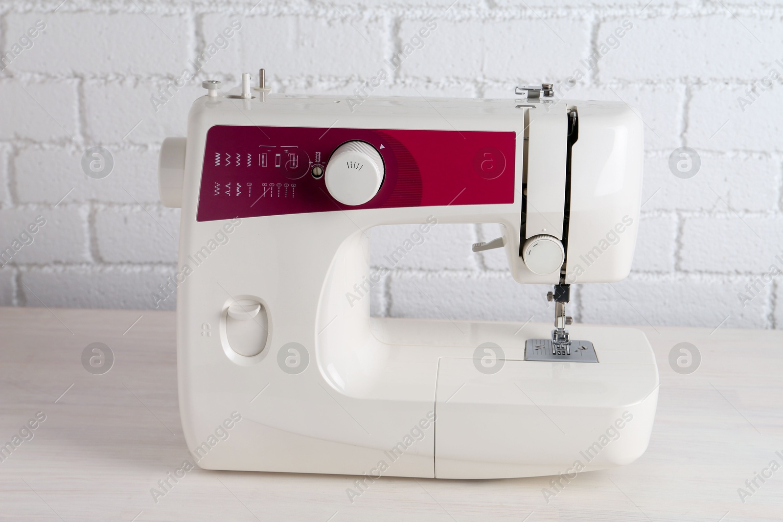 Photo of Modern sewing machine on wooden table near white brick wall