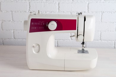 Modern sewing machine on wooden table near white brick wall