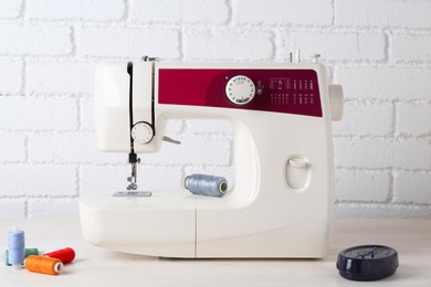 Photo of Modern sewing machine and craft accessories on wooden table near white brick wall