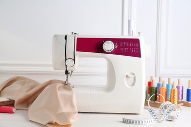 Photo of Sewing machine and craft accessories on white wooden table indoors