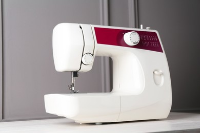 Sewing machine on white wooden table near gray wall