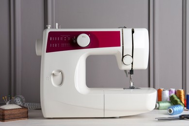 Photo of Sewing machine and craft accessories on white wooden table near gray wall