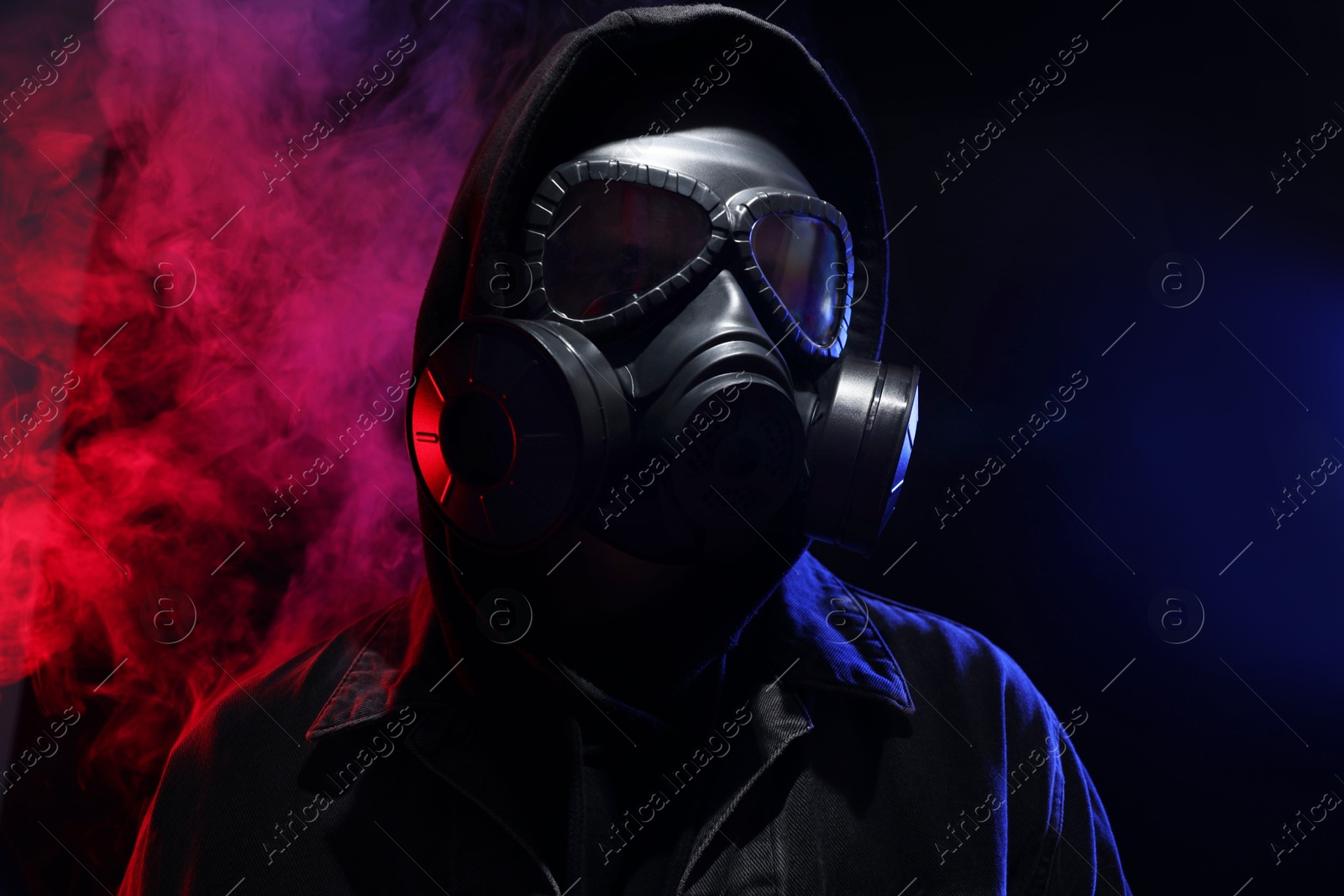 Photo of Man wearing gas mask in color lights and smoke on black background