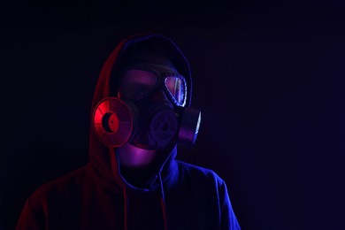 Man wearing gas mask in color lights on black background. Space for text