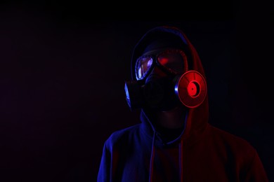 Photo of Man wearing gas mask in color lights on black background. Space for text